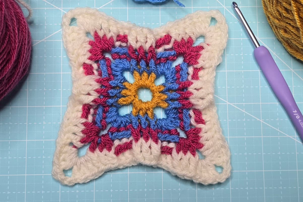 The Russian granny square with combinations of gold, blue, magenta, and white yarns