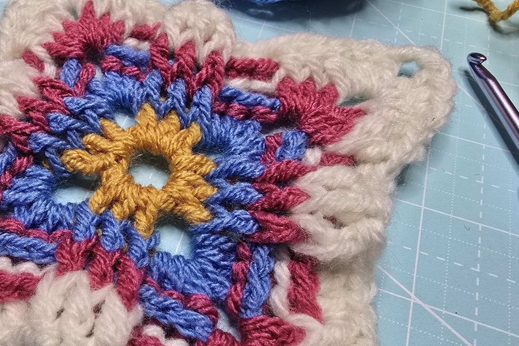 A closer Russian granny square with combinations of gold, blue, magenta, and white yarns showcasing how the front and back post double makes the square looks stunning